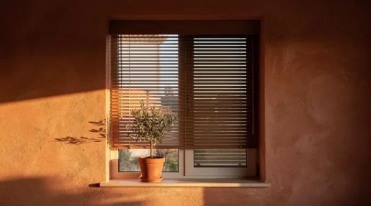 Fachada de una vivienda mediterránea española con una persiana de madera entreabierta filtrando la luz dorada del atardecer