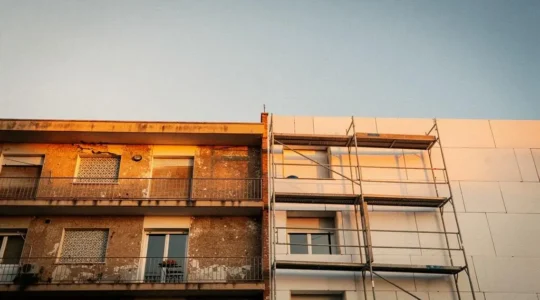 Fachada de un edificio residencial antiguo español a medio renovar, con andamios y luz cálida de atardecer, simbolizando la transformación integral del inmueble