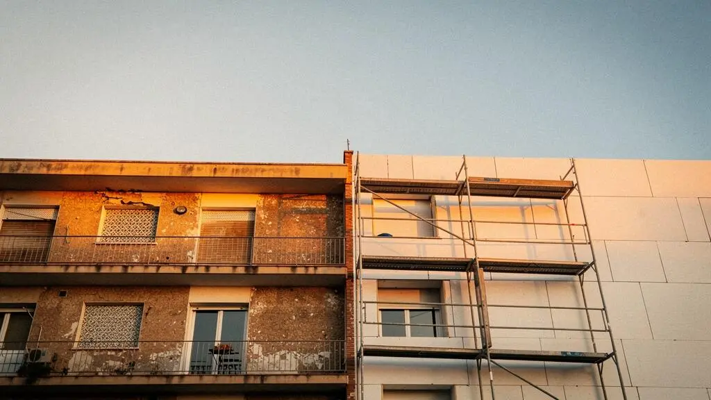 Fachada de un edificio residencial antiguo español a medio renovar, con andamios y luz cálida de atardecer, simbolizando la transformación integral del inmueble