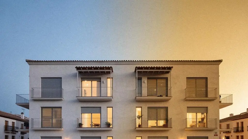 Fachada de una vivienda española moderna al atardecer con luz cálida en las ventanas, simbolizando el confort térmico equilibrado en invierno y verano